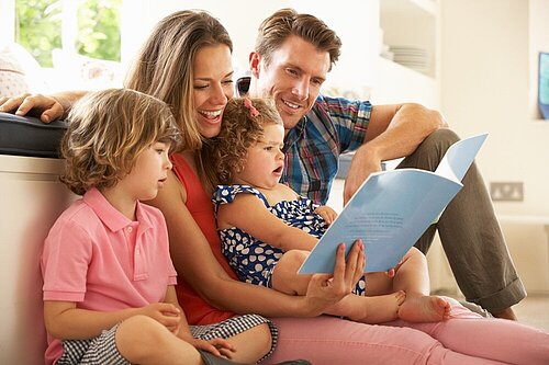 A mother, father, brother and sister sitting reading a book.